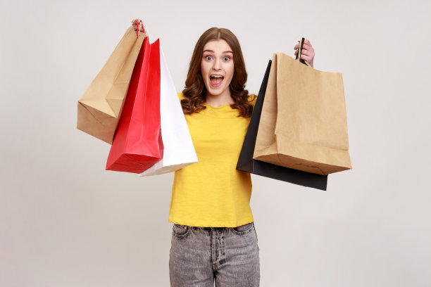 心满意足的少女穿着黄色休闲风格的T恤，手里拿着购物纸袋，兴奋地拿着商场的折扣、好货。图片下载