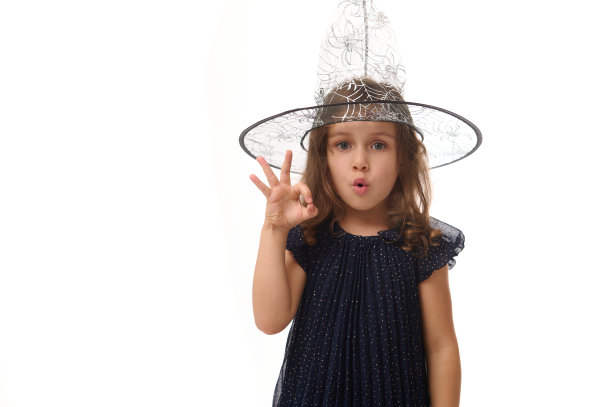 孤立的、齐腰的小女巫肖像，戴着巫师帽，穿着时髦的狂欢节服装，手势，用手指显示OK的标志。白色背景下的万圣节概念图片下载