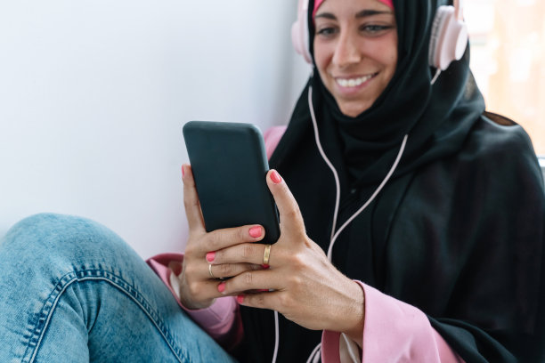 年轻的穆斯林妇女戴着头巾在室内使用智能手机。图片下载