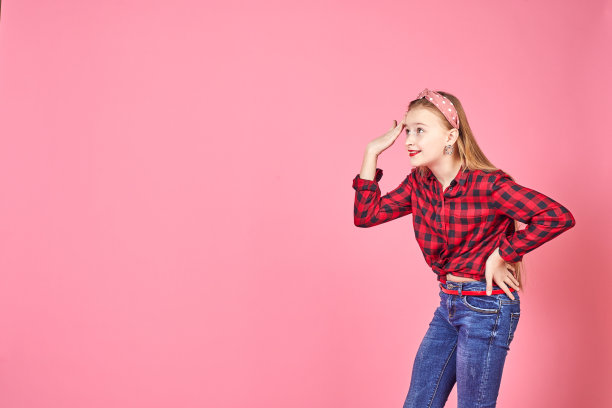 白人女大学生摆姿势，用手指。正面的年轻女子看着相机在粉红色的背景。图片下载