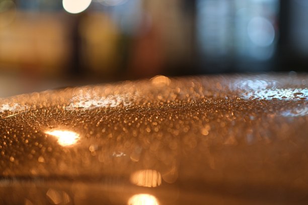 夜晚城市的彩灯在雨滴滴在金属车顶上图片下载