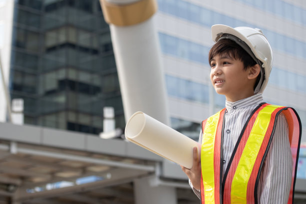 小男孩戴着工程头盔，手里拿着城市建筑图纸。启发孩子未来的理念。图片下载