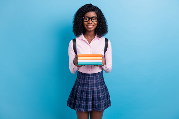 年轻的黑人女学生的照片快乐积极的微笑持有书籍教育学习孤立在蓝色背景图片下载