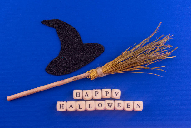 黑色女巫帽，扫帚和快乐的万圣节字母在蓝色的背景。图片下载