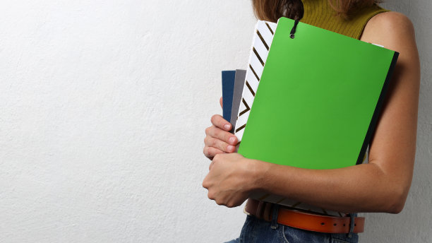 学生拿着彩色的笔记本对着空白的白色墙壁。空的空间图片下载