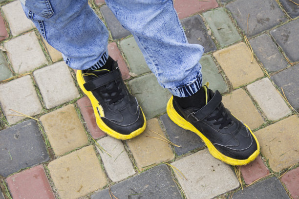 一个孩子穿着黄色的运动鞋在彩色的铺路石上，穿着运动鞋图片下载