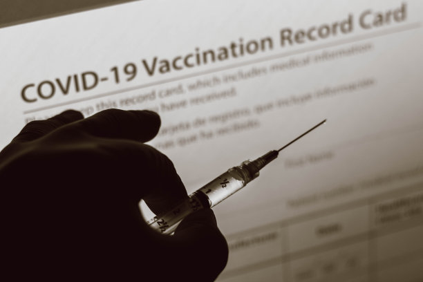 照片中，手持医疗注射器的手在背景屏幕上显示了新冠疫苗记录卡图片下载