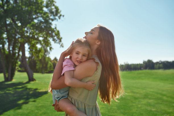快乐的年轻母亲抱着她可爱的小女儿，闭着眼睛微笑，一起在夏天的公园里度过时光图片下载
