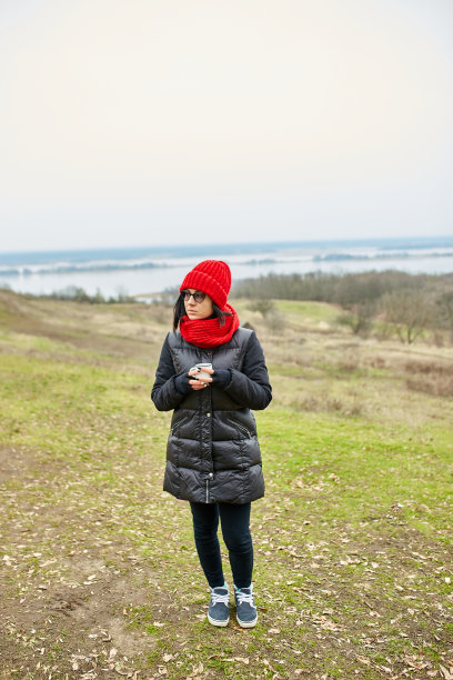 戴着红帽子和围巾的女人，在户外用金属杯喝茶图片下载