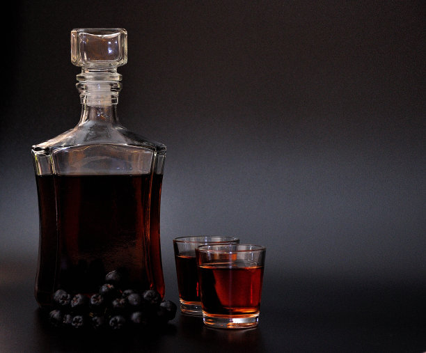 自制的苦果利口酒，烈酒放在两个玻璃杯和一个玻璃瓶里，黑色背景，旁边是一串成熟的浆果。图片下载