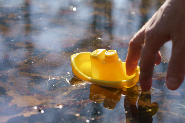 人的手推黄色的玩具船在大水坑图片下载