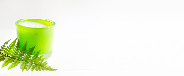 白色背景上带有蕨类植物和自然香味的绿色蜡烛。芳香疗法，放松，身体护理，和谐。副本的空间。横幅图片下载