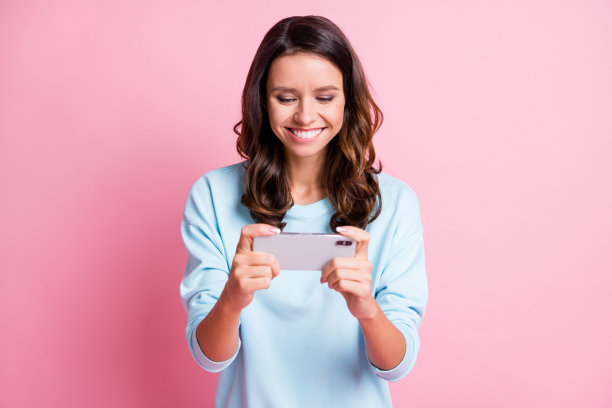 照片的年轻有吸引力的女人快乐积极的微笑玩游戏智能手机隔离在柔和的颜色背景图片下载