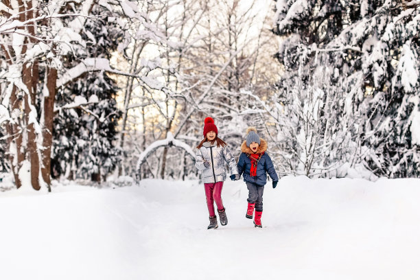 冬天的下午，微笑着的孩子们快乐地跑过白雪覆盖的公园图片下载
