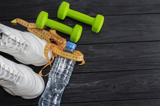 黑色背景上有一双有哑铃和一瓶水的跑鞋。健康的生活方式图片下载