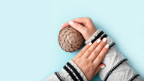 节日的女人用白色修指甲。手捧着金灿灿的金球。舒适的气氛。壮观的指甲与白色装饰。柔和的颜色,简约的概念。圣诞节修指甲的点子，大横幅。图片下载