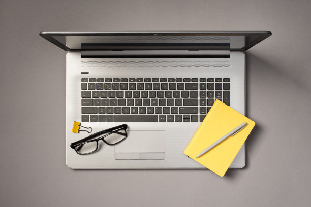 顶视图照片的眼镜黄色夹笔和黄色记事本上打开的灰色笔记本电脑孤立的灰色背景图片下载