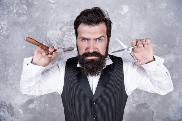 英俊野蛮的男人理发师与胡子举行理发店复古剃须刀片和剪刀，发廊。图片下载