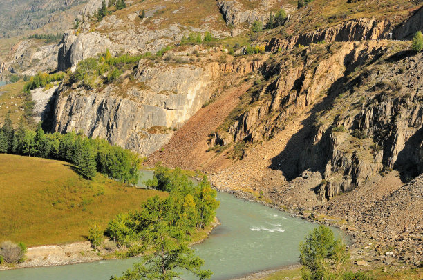 一条风景如画的绿松石河流的河床的弯道，它流淌在高高的岩石悬崖脚下。图片下载