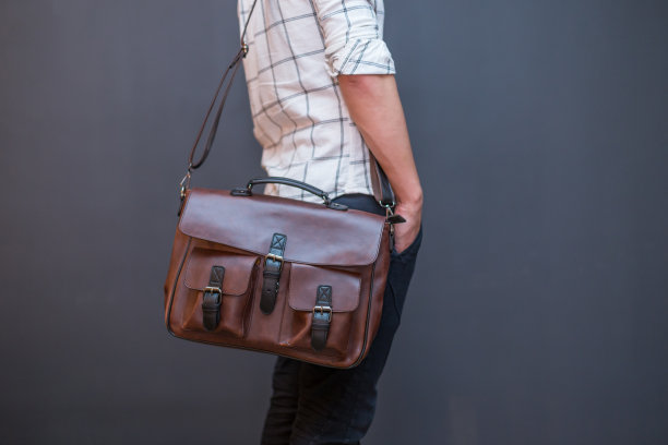 男人手里拿着棕色的皮革邮差包图片下载