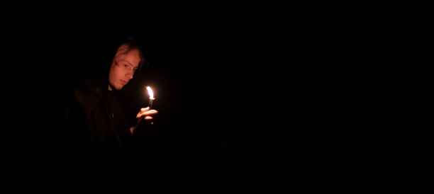 沉着神秘的讲故事少年手中拿着蜡烛，万圣节广告概念全景图片，以黑色背景空间为文本或复制图片下载