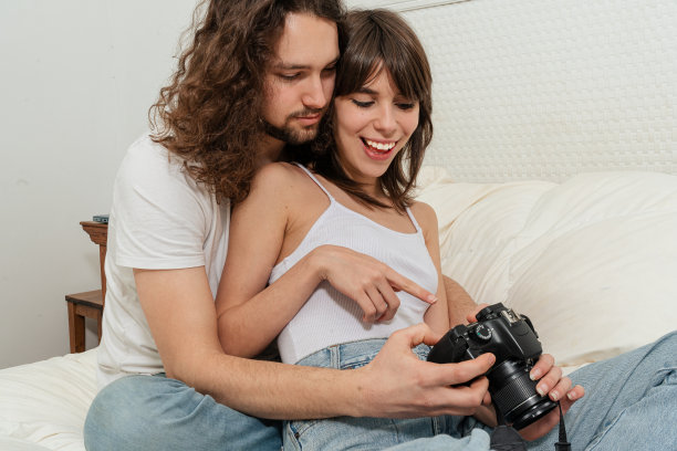 一对夫妇坐在家里的床上，用单反相机看照片。图片下载