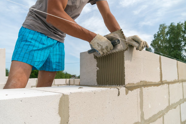 施工人员用带槽的镘刀将水泥混合物涂抹在砌块的一侧。建造房屋的概念图片下载