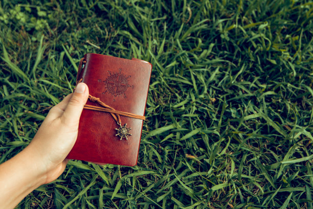 他手里拿着一本棕色的皮革笔记本，背景是绿色的草地图片下载
