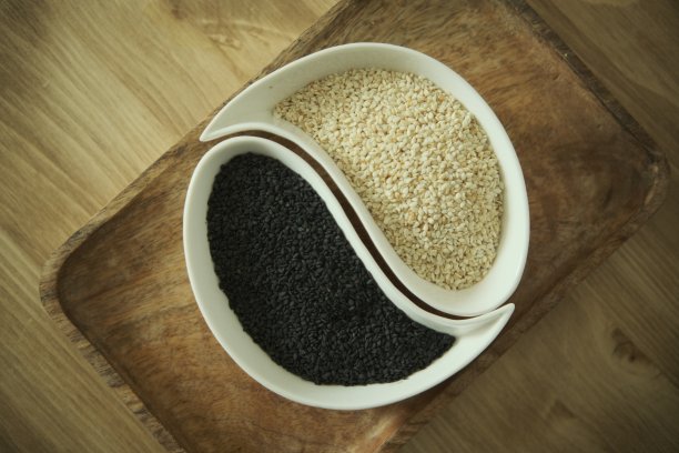白芝麻和黑芝麻放在白盘子里。木制的桌子。软选择性模糊背景图片下载