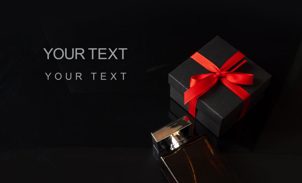 香水瓶旁边的黑色礼品盒与红色蝴蝶结丝带在黑暗的背景。黑色星期五促销，圣诞礼物或情人节礼物概念。带有复制空间的横幅。图片下载