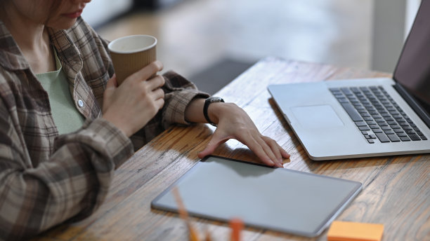 剪裁拍摄的女性创意设计师喝咖啡和使用数字平板电脑。图片下载