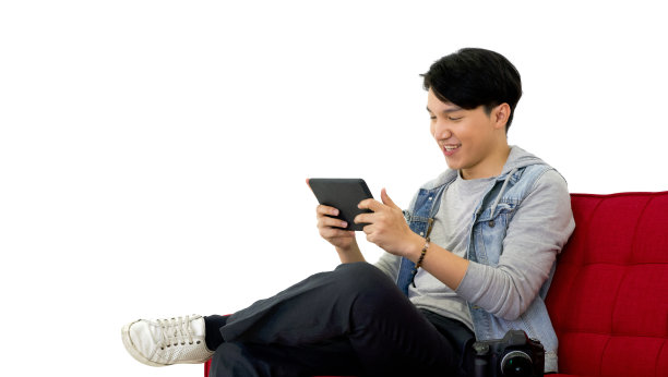 年轻的亚洲摄影师微笑着观看平板电脑屏幕上的照片，坐在红色的沙发上。摄影棚里的工作氛围图片下载