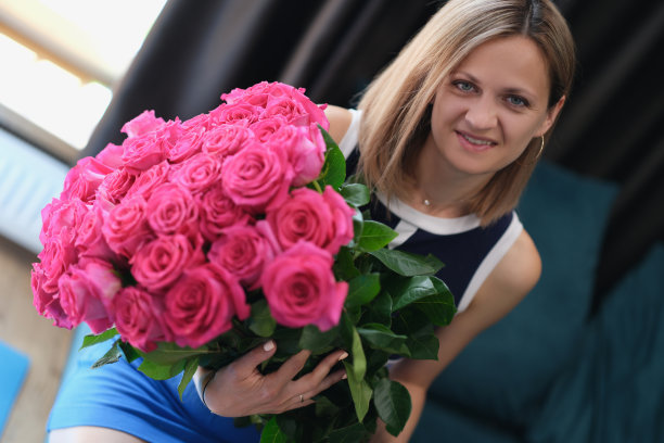 一个年轻的女人坐在沙发上，手里拿着一大束玫瑰花图片下载