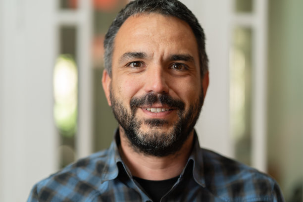 正面照片:白种人成熟男人，留着胡子，留着短发，面带微笑，站在办公室或家里，穿着衬衫，看着镜头图片下载