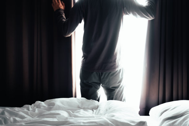 一个男人的剪影拉开窗帘，床图片下载