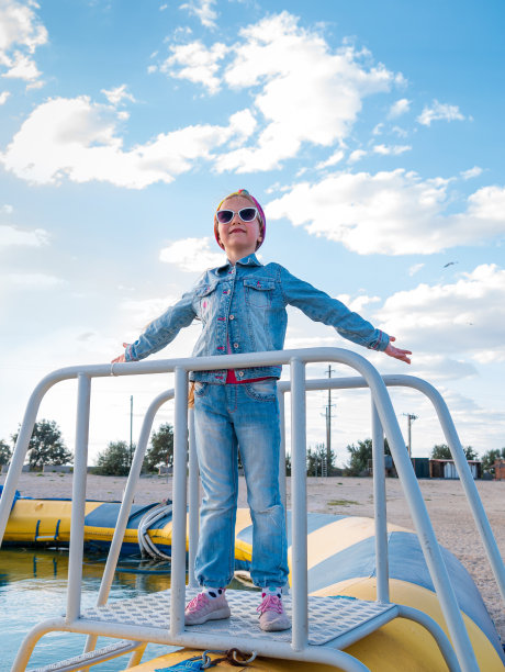 金发小女孩举起双臂，蓝色的云天背景。快乐的孩子微笑着在空中飞翔。生活的照片图片下载