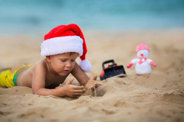 快乐的男孩戴着圣诞老人的帽子在沙滩上玩耍。圣诞节的孩子在海边休息。本空间图片下载