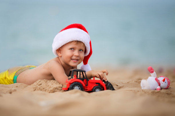 戴着圣诞老人帽子的快乐男孩在海滩上玩玩具车。圣诞节的孩子在海边休息。本空间图片下载
