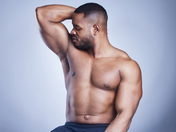 摄影棚拍摄了一个英俊的年轻人在蓝色背景下闻他的腋窝图片下载