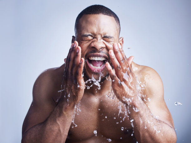 摄影棚拍摄了一个英俊的年轻人洗他的脸在灰色的背景图片下载