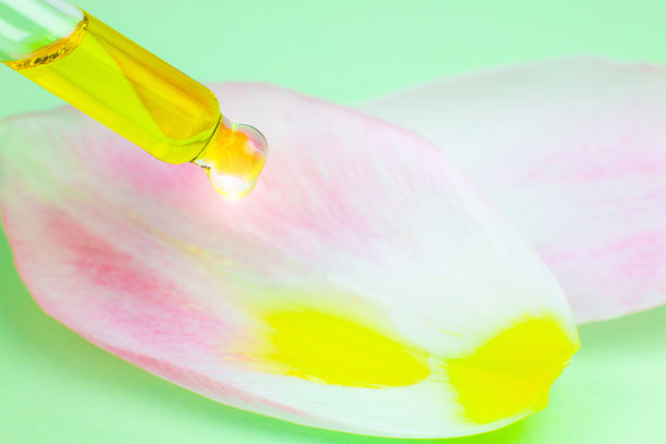 用吸管吸化妆油，绿色背景。关闭液体滴在花瓣上从粉红色郁金香花。美容、医药、保健理念。宏观照片。自然,生态化妆品。图片下载