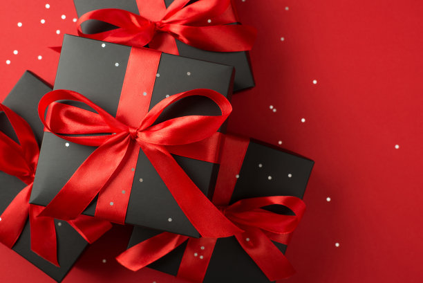 顶视图照片的堆叠黑色礼品盒与红色蝴蝶结和亮片在孤立的红色背景与copyspace图片下载