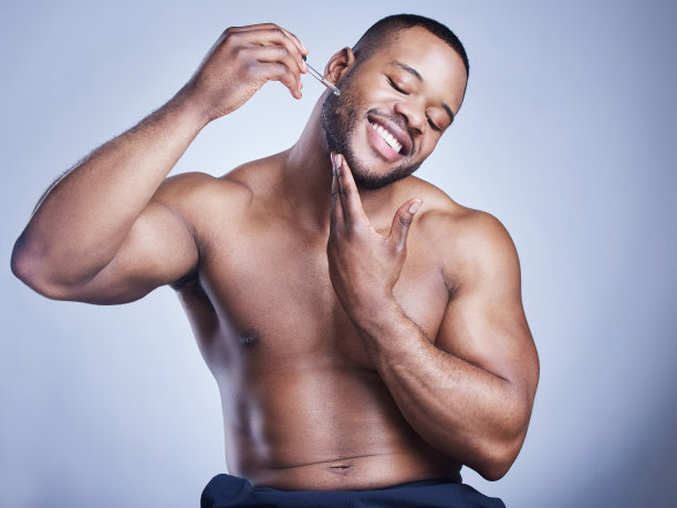 摄影棚拍摄的一个英俊的年轻男子在他的脸上涂血清对蓝色的背景图片下载