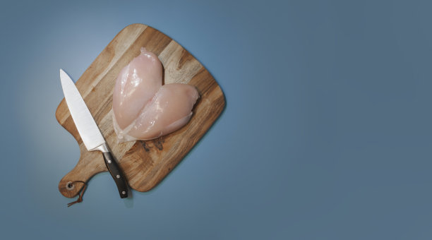 整块生鸡胸肉放在砧板上，用菜刀。在蓝色背景上。本空间图片下载