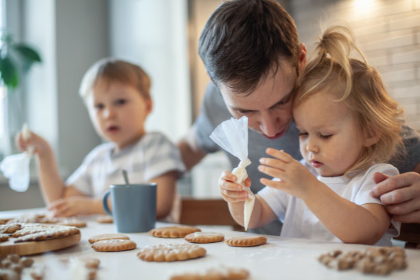 爸爸和孩子们在家装饰圣诞姜饼。一个男孩和一个女孩在饼干上涂上糖霜。新年的装饰品，圣诞树的树枝图片下载