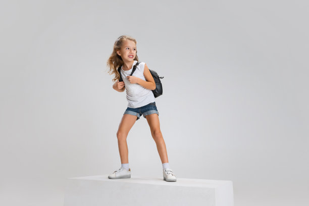 身着休闲装微笑的女孩全身肖像，站在白色工作室背景上孤立的大盒子上。快乐的童年的概念。图片下载