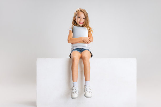 可爱的小女孩的肖像，穿着休闲装坐在大盒子孤立在白色的工作室背景。快乐的童年的概念。图片下载