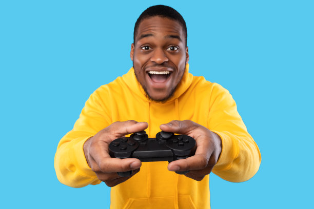 非洲裔美国人玩电子游戏，用操纵杆摆姿势，蓝色背景图片下载
