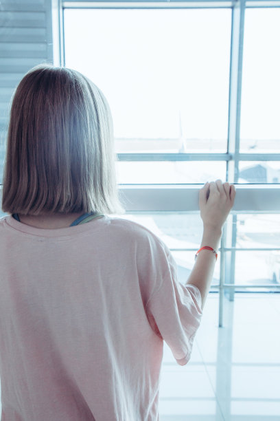 一个十几岁的女孩站在机场，透过飞机的登机口窗户往外看图片下载