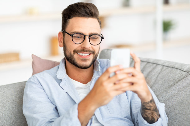 国内休闲。快乐的家伙使用智能手机，休息在客厅内部的沙发，复制空间图片下载